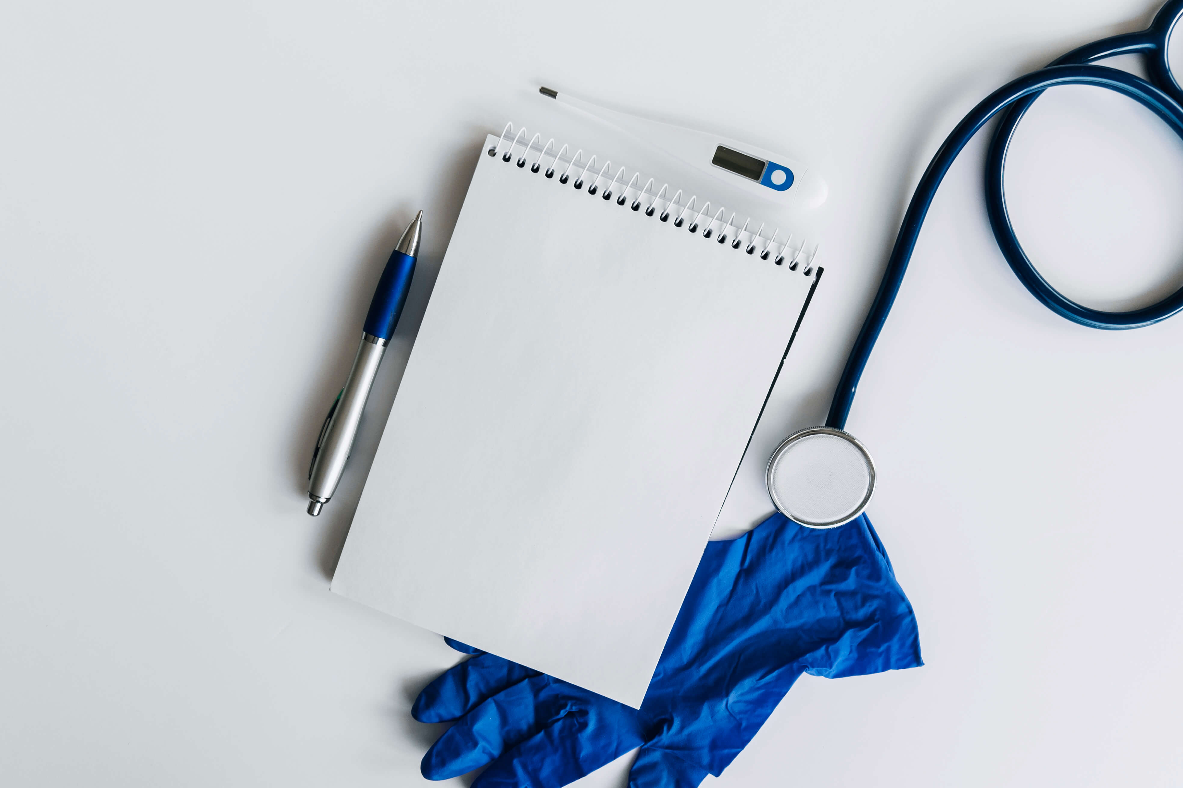 elevated view spiral notepad pen stethoscope thermometer gloves white backdrop